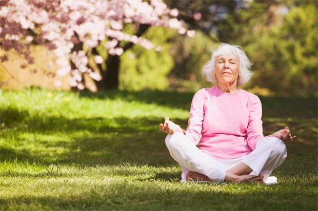 An elderly woman meditates in nature under sakura