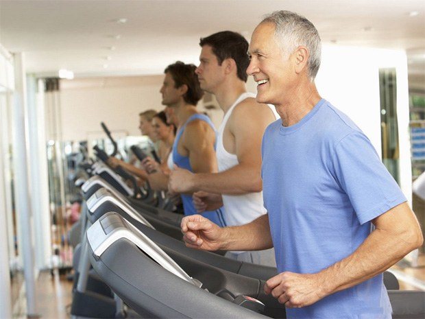 An elderly man in the gym walks on a treadmill